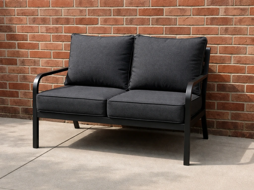Warm charcoal and warm black metal patio loveseat with cushions against a red brick wall.
