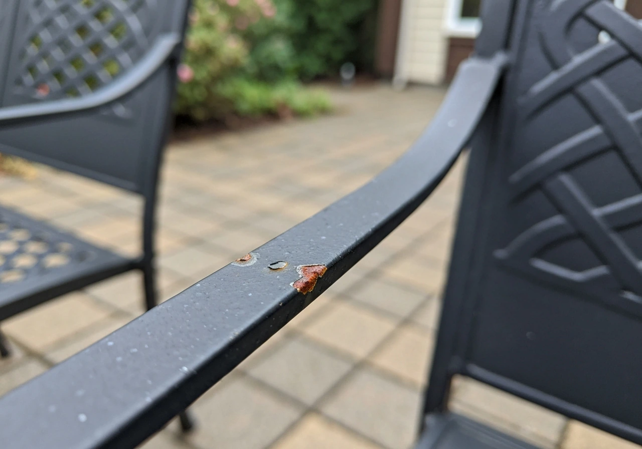 Close-up of wrought iron patio furniture where a chipped coating shows early rust next to intact paint.